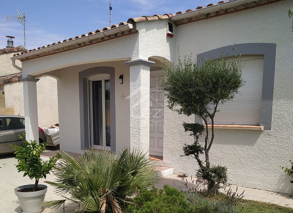 Maison blanche avec porte et fenêtre, plantes devant