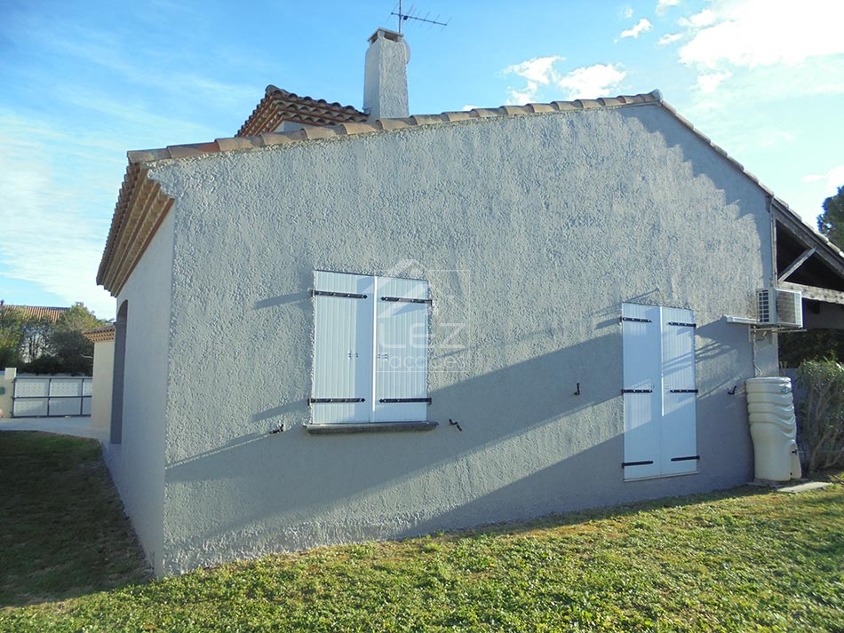 Maison blanche avec volets, toit en tuiles, jardin vert.