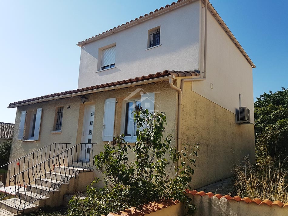 Maison à deux étages avec fenêtres blanches et toit en tuiles rouges.